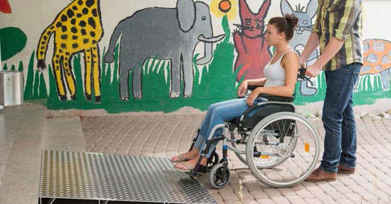 Junge schiebt Mädchen im Rollstuhl über eine Keilbrücke