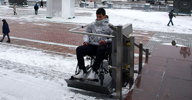 Im Winter transportiert ein Plattformlift einen Jungen im Rollstuhl