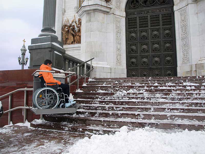 Treppenplattformlift für den Rollstuhl überwindet Freitreppe an winterlicher Kirche 